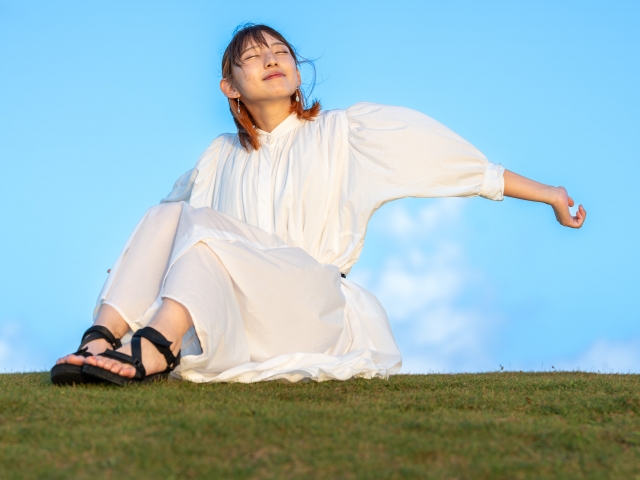 青空の下、芝生に座り腕を伸ばす女性